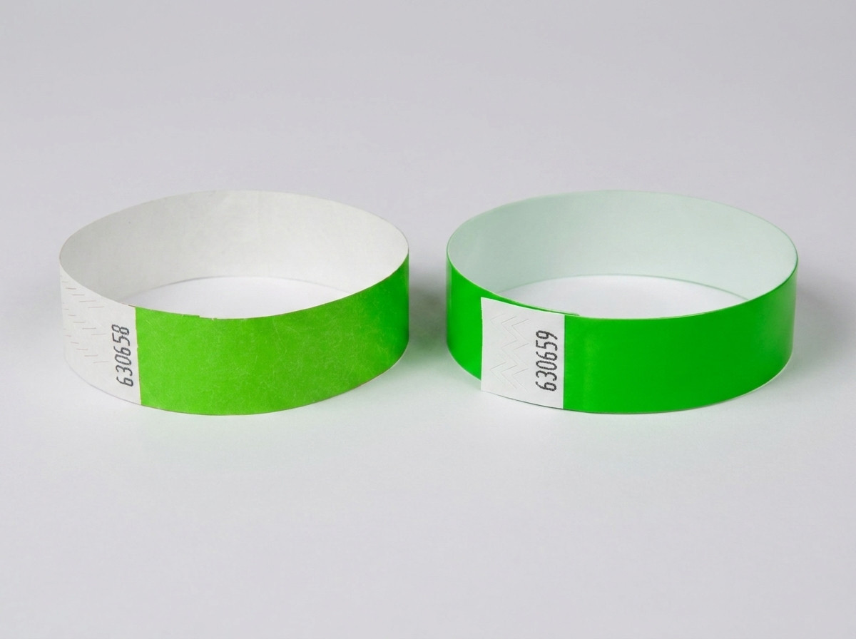 Comparação lado a lado de uma pulseira Tyvek branca com código de barras impresso e de uma pulseira de identificação colorida com código de barras, pousadas sobre uma mesa de festival